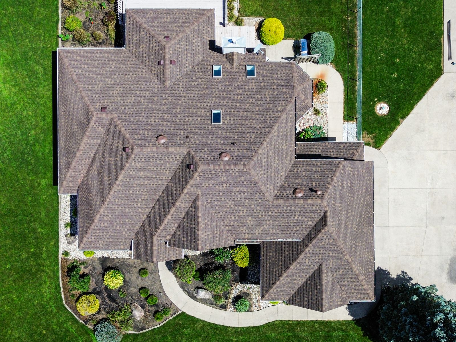 Top-down aerial of a completed warm brown architectural shingle roof with three skylights and multiple hip planes — Bellefontaine, Ohio