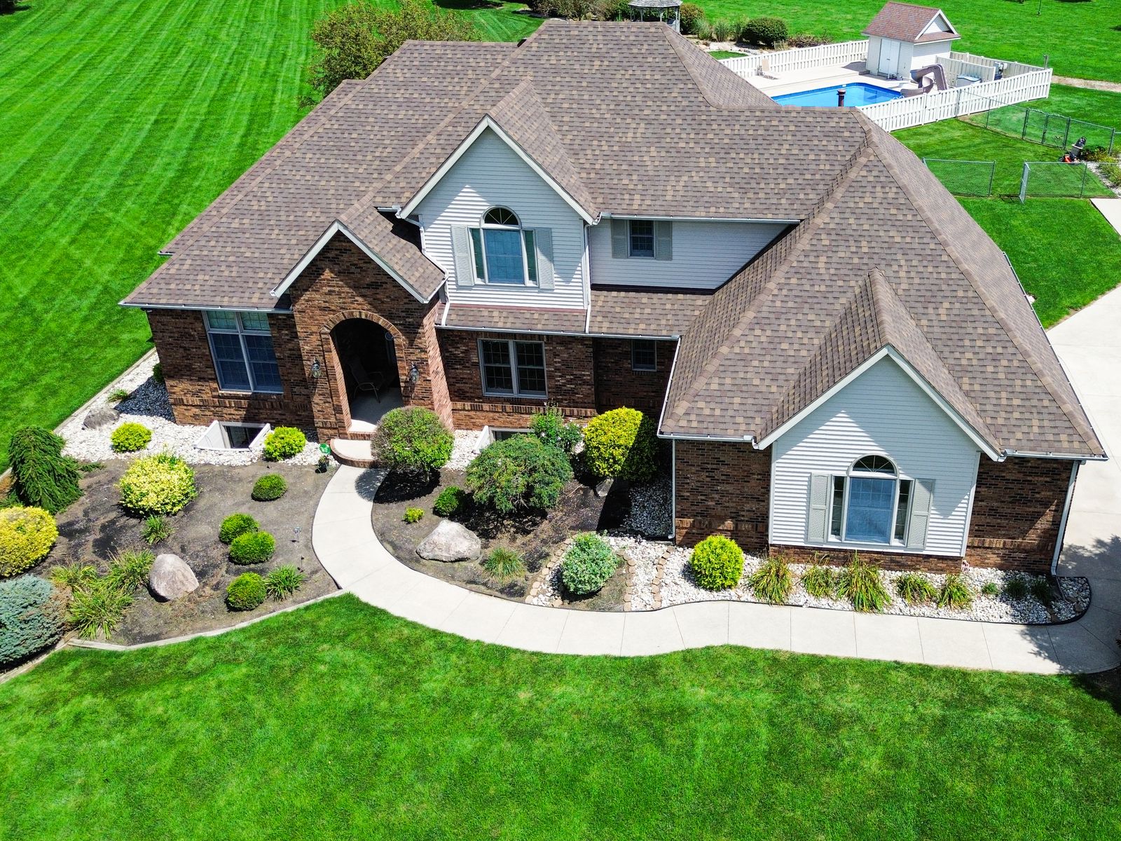 Completed warm brown GAF Timberline HDZ roof on a large brick home with arched entry and detached carriage building — Bellefontaine, Ohio
