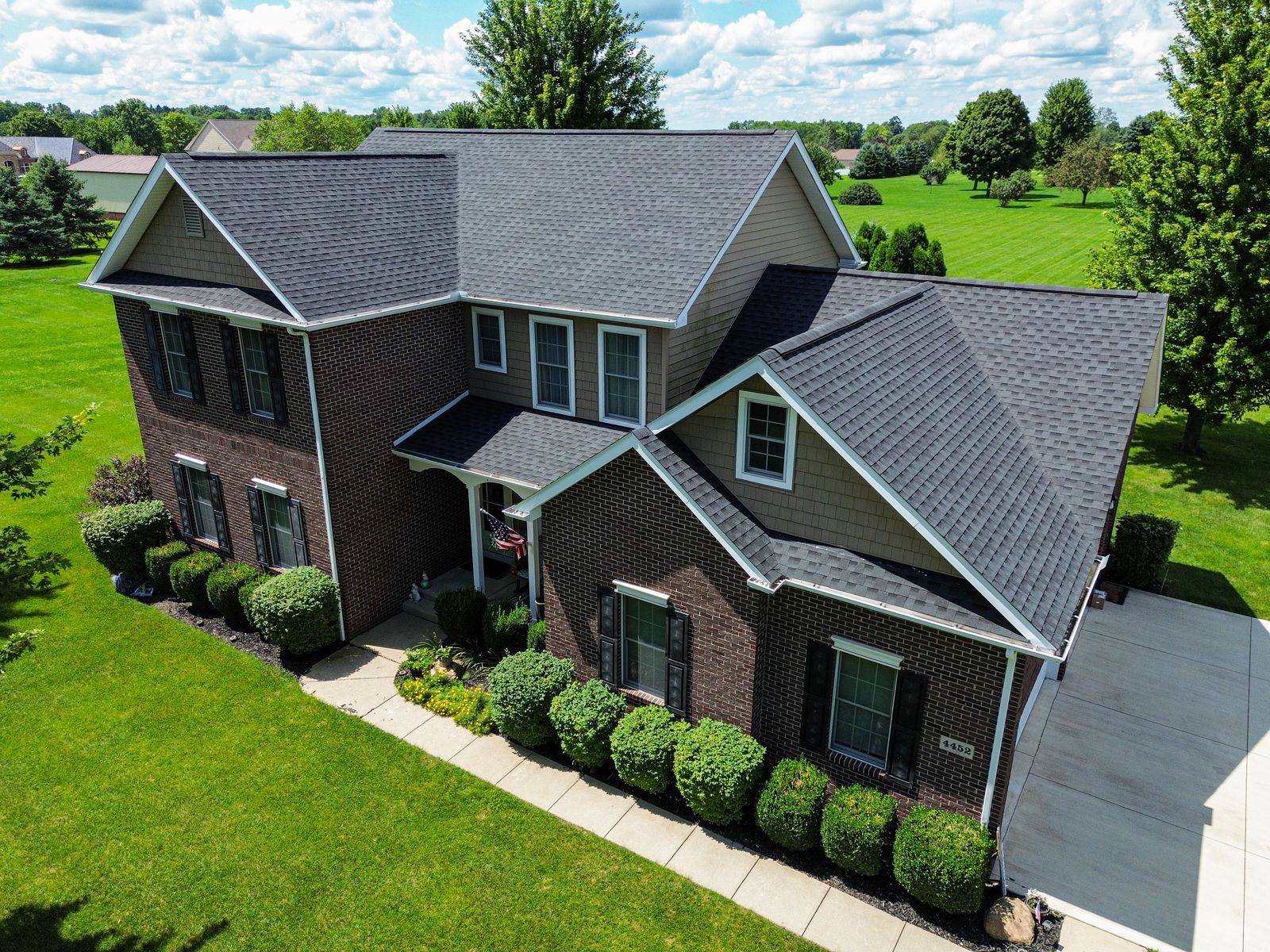 Front-right aerial of the completed Charcoal GAF roof over brick and cedar-shake gables — Bellefontaine, Ohio