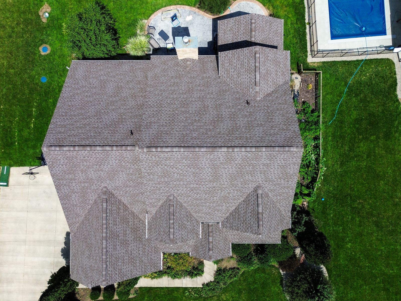 Top-down aerial of a completed architectural shingle roof on a Craftsman home with multiple gable peaks and a rear pool — Bellefontaine, Ohio
