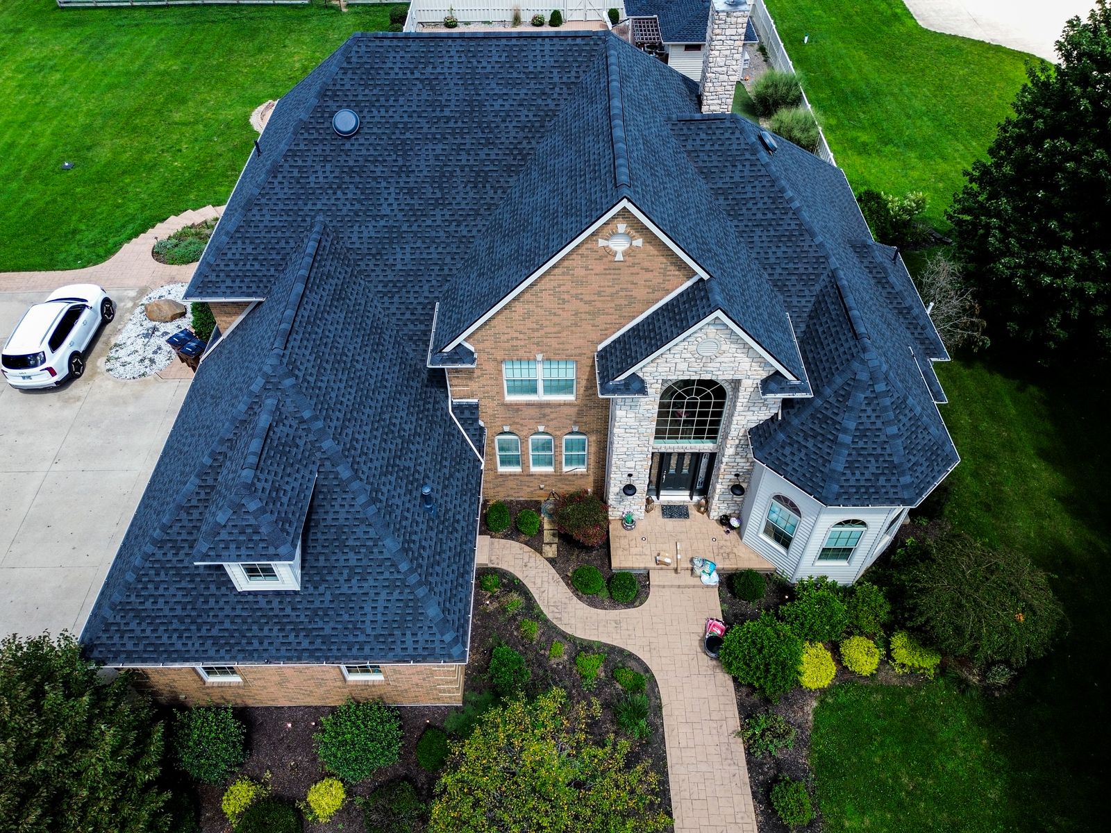 Completed dark GAF Timberline HDZ roof on a large brick-and-stone home with an arched entry and octagonal turret — Bellefontaine, Ohio