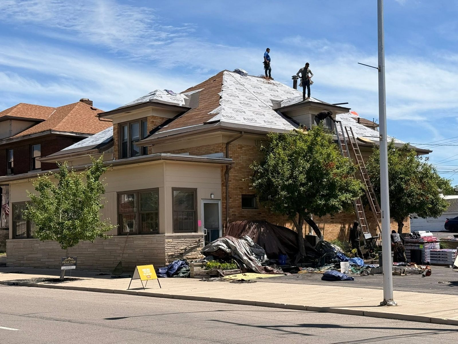 Peak One crew installing ABC ProGuard synthetic underlayment on a hip roof at a downtown commercial building — Bellefontaine, Ohio