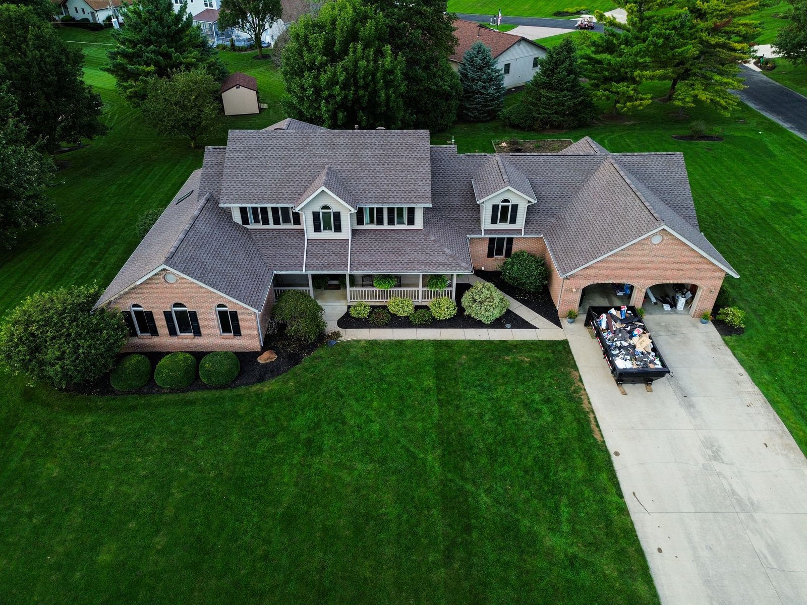 Wide aerial of the completed roof replacement on a brick home with wraparound porch — Hardin County, Ohio